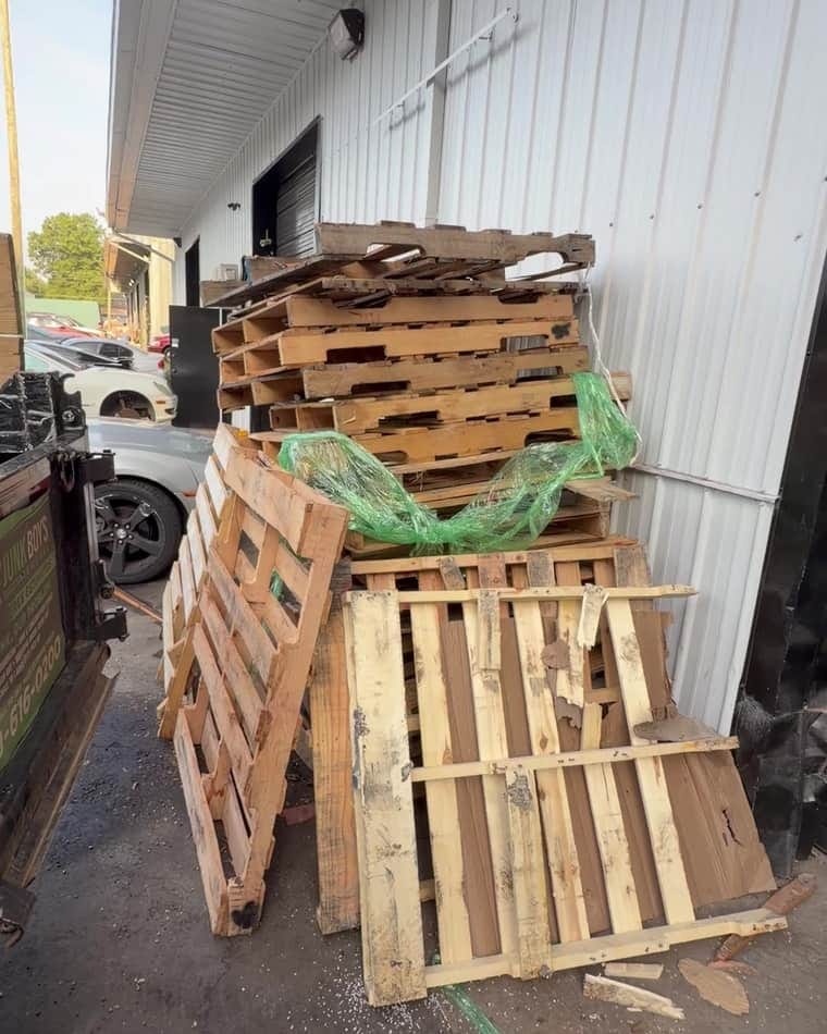 Stacked wooden pallets and debris piled against a warehouse loading dock before removal