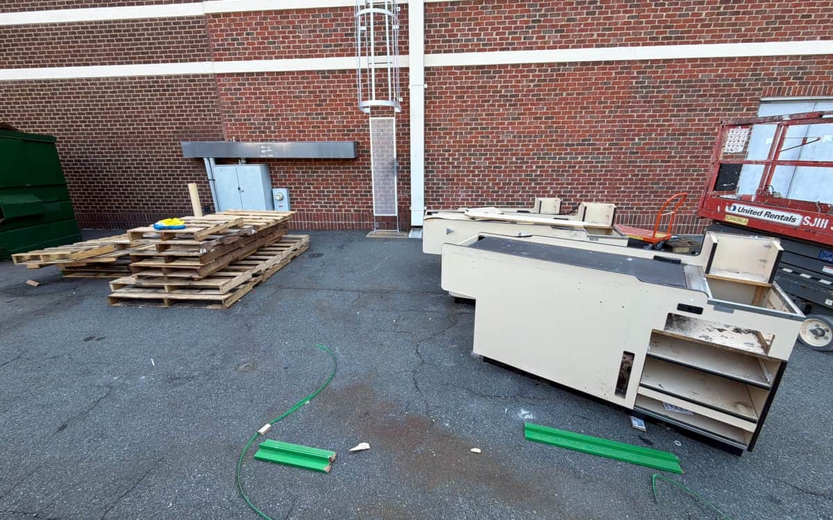 Old retail checkout counters, shelving units and stacked pallets staged behind a commercial building before removal
