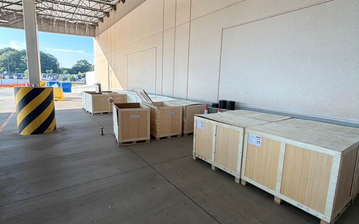 A row of large wooden shipping crates staged along a warehouse loading canopy before removal