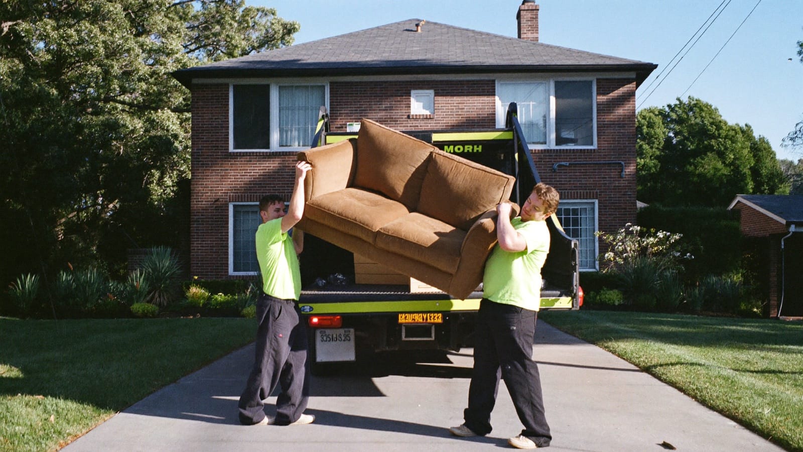 Two Junk Boys crew members lifting a sectional into the truck in a Charlotte driveway